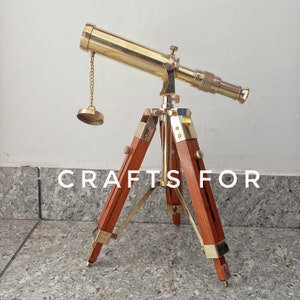 May include: A brass telescope with a wooden tripod. The telescope has a chain attached to the top and a brass cap on the end of the chain. The tripod is made of dark brown wood.