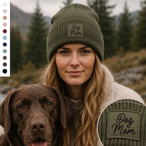 Könnte beinhalten: Eine olivgrüne, gerippte Strickmütze mit einem quadratischen Aufnäher auf der Vorderseite, der den Text Dog Mom in schwarzer Schreibschrift zeigt. Die Mütze hat ein umgeschlagenes Bündchen und ein strukturiertes Strickmuster im gesamten Stoff.