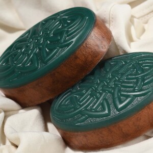 May include: Two green and brown oval-shaped soaps with a Celtic knot design.