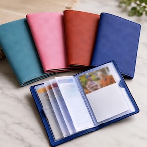 Pode incluir: Uma coleção de porta-cartões retangulares em azul-petróleo, rosa, castanho e azul. Um porta-cartões azul está aberto, exibindo várias mangas de plástico transparente para organizar cartões, com uma pequena fotografia visível.