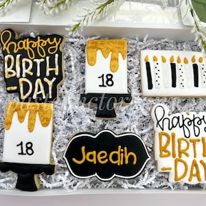 May include: A set of six decorated sugar cookies with a black and gold colour scheme. The cookies feature the words "Happy Birthday" and the number "18". One cookie is a black chalkboard with the name "Jaedin" written in gold.