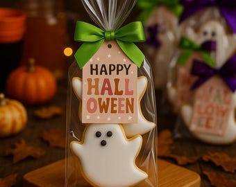 May include: A clear cellophane bag tied with a green ribbon contains two ghost-shaped cookies. A tag with the words "HAPPY HALLOWEEN" is attached. The cookies are white with black eyes and a yellow outline. The background includes pumpkins and fall leaves.