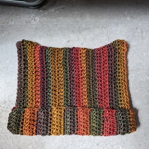 Puede incluir: Un gorro de punto de crochet a rayas en tonos naranja, marr&oacute;n, verde y rojo.