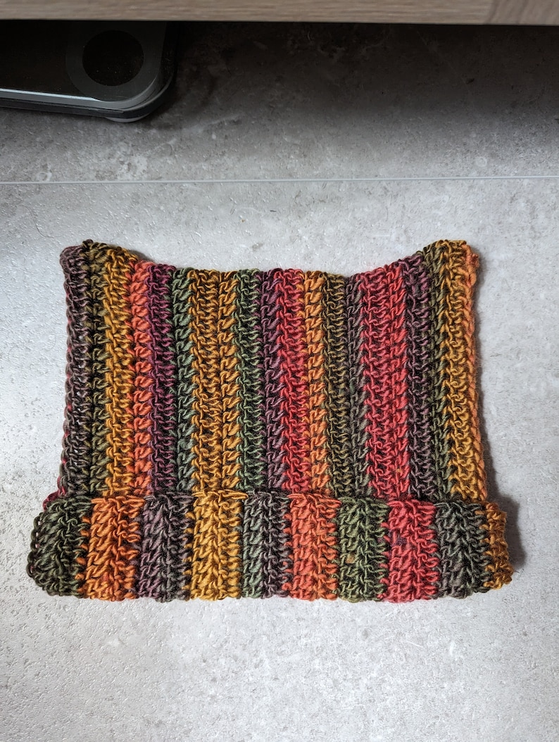 Puede incluir: Un gorro de punto de crochet a rayas en tonos naranja, marr&oacute;n, verde y rojo.