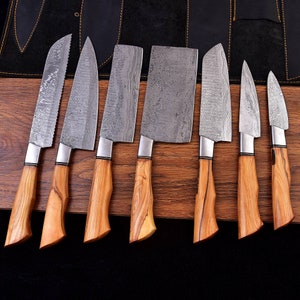 Può includere: Un set di sette coltelli da cucina con manici in legno e lame in acciaio decorate. Le lame hanno forme diverse, tra cui un coltello da pane seghettato, una mannaia e diversi coltelli da chef. I manici sono marrone chiaro e le lame argentate.