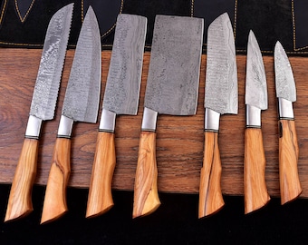May include: A set of seven kitchen knives with wooden handles and patterned steel blades. The blades vary in shape, including a serrated bread knife, a cleaver, and several chef's knives. The handles are a light brown color, and the blades have a silver finish.
