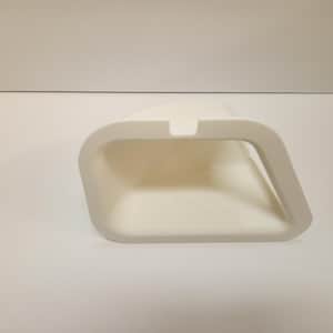 May include: A white, angled, rectangular container with a curved handle. The container has a recessed area on the top. The object is made of a solid, opaque material and sits on a white surface.
