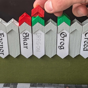 May include: A row of light gray, pointed, vertical markers with textured surfaces. Each marker features a name printed in black ink, including Faenor, Skar, Dragon, Grog, and Creed. Some markers have red or green triangular toppers attached.