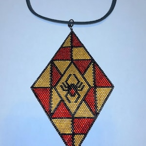 May include: A beaded pendant necklace with a geometric design. The pendant is a diamond shape with red, gold, and black beads. A black spider is in the center. The necklace has a black cord.