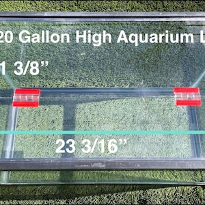 May include: A clear glass 20-gallon high aquarium lid with black trim. The lid measures 28.89 cm wide and 58.89 cm long. Two red clips secure the lid. The text "20 Gallon High Aquarium Lid" is visible.
