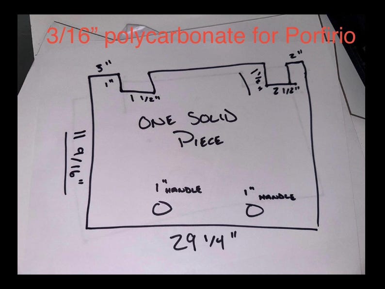 May include: A hand-drawn diagram on white paper with black ink, featuring measurements in inches. The text reads "3/16" polycarbonate for Porto", "ONE SOLID PIECE", and "1" HANDLE". The overall dimensions are 29 1/4" x 11 9/16".