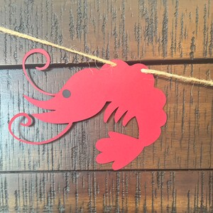以下が含まれることがあります： 赤い紙で切り抜かれたエビの飾り。尻尾が巻いていて、紐で吊るされています。