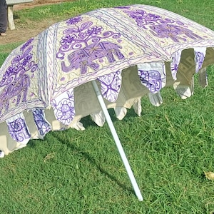 May include: A white and purple patterned umbrella with embroidered elephants. The umbrella is open and the white pole is visible.