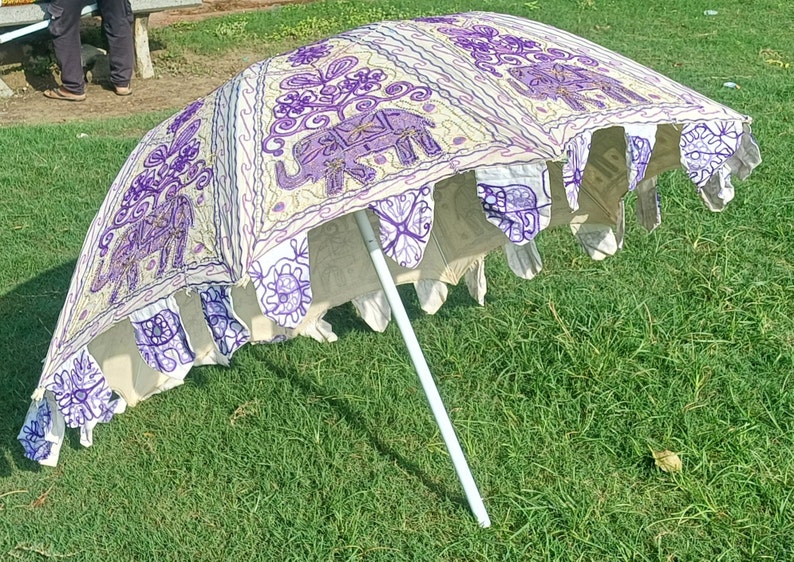 May include: A white and purple patterned umbrella with embroidered elephants. The umbrella is open and the white pole is visible.