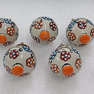 May include: Five ceramic knobs with a white background and floral designs in shades of orange, red, blue, and white. Each knob has a small orange circle in the center.