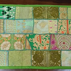 K&ouml;nnte beinhalten: Ein gr&uuml;nes Patchwork-Wurfkissen mit verschiedenen floralen und geometrischen Mustern in Gr&uuml;n-, Gold- und Rosat&ouml;nen.