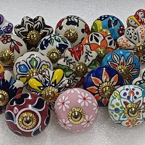 Op de afbeelding: Een verzameling van 20 kleurrijke keramische ladeknopjes met bloem- en geometrische ontwerpen. De knopjes zijn rond en hebben een gouden metalen accent in het midden.