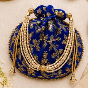 Peut inclure: Une pochette à cordon en velours bleu roi ornée de broderies au fil d'or et de sequins. Le sac est décoré de plusieurs rangs de perles artificielles couleur crème et de perles métalliques dorées, terminés par des pompons dorés en forme de cloche.
