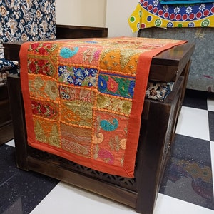 K&ouml;nnte beinhalten: Ein Holztisch mit einem bunten Patchwork-L&auml;ufer. Der L&auml;ufer besteht aus verschiedenen Stoffen und hat viele Stickereien. Der Tisch ist dunkelbraun und hat ein geschnitztes Design an den Beinen.