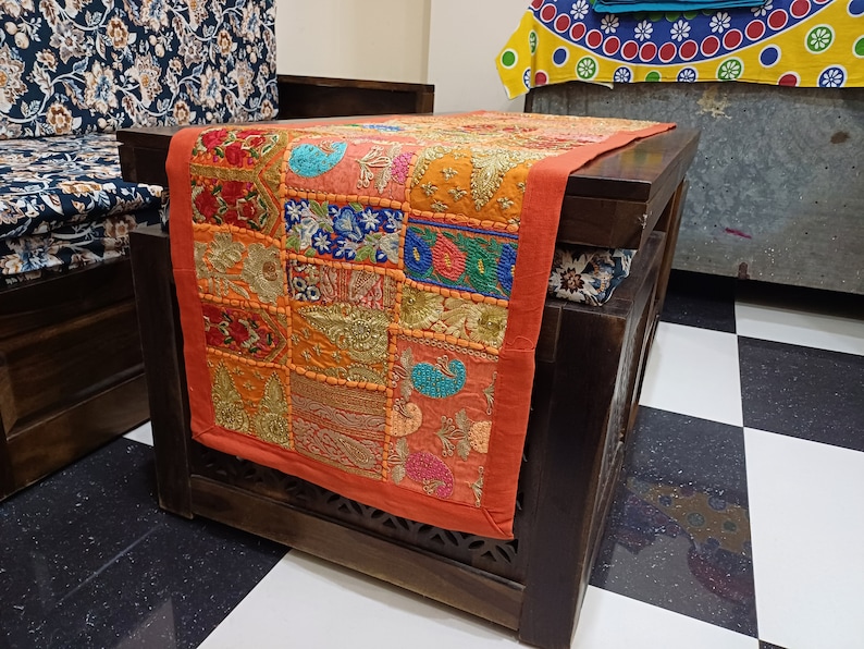 K&ouml;nnte beinhalten: Ein Holztisch mit einem bunten Patchwork-L&auml;ufer. Der L&auml;ufer besteht aus verschiedenen Stoffen und hat viele Stickereien. Der Tisch ist dunkelbraun und hat ein geschnitztes Design an den Beinen.