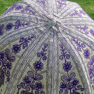 May include: A white and purple patterned umbrella with a beaded trim. The umbrella is made of fabric and has a traditional design.