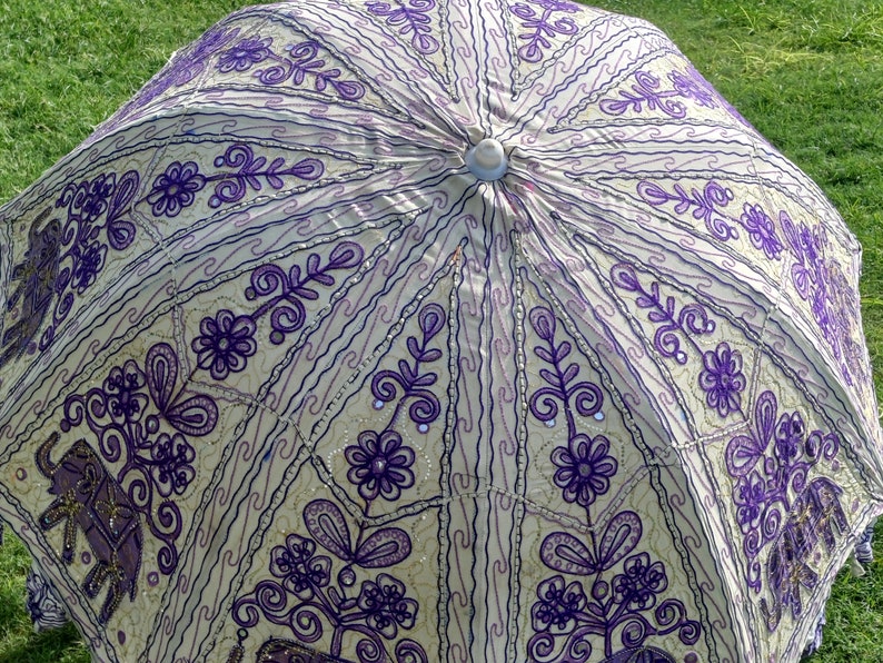 May include: A white and purple patterned umbrella with a beaded trim. The umbrella is made of fabric and has a traditional design.