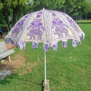 May include: A white and purple umbrella with an embroidered elephant design. The umbrella is open and has a white pole.