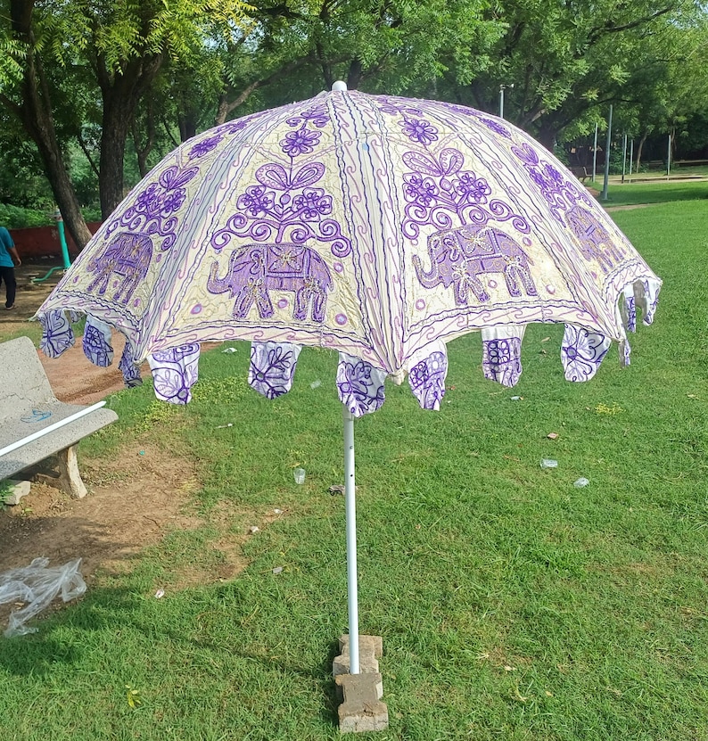May include: A white and purple umbrella with an embroidered elephant design. The umbrella is open and has a white pole.
