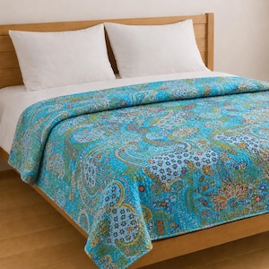 Könnte beinhalten: Eine gesteppte Tagesdecke mit einer leuchtend türkisfarbenen Basis und einem komplexen, mehrfarbigen Paisley- und Blumenmuster in Gelb-, Orange- und Blautönen. Die Decke liegt auf einem Bett mit zwei weißen Kissen und einem hölzernen Kopfteil.