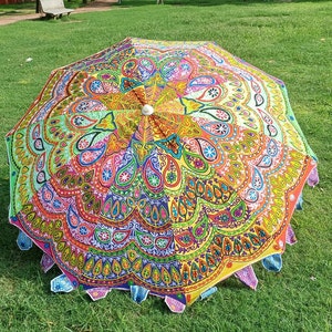 May include: A circular parasol featuring a vibrant, multi-colored mandala pattern with intricate paisley and floral motifs in shades of yellow, pink, blue, green, and orange. The edge is finished with small, decorative fabric triangular accents.