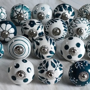 Op de afbeelding: Een verzameling van 18 keramische ladegrepen met een witte basis en tealblauwe ontwerpen. De grepen hebben verschillende patronen, waaronder bloemmotieven, geometrische en abstracte ontwerpen.