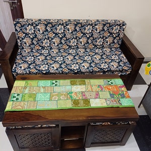 K&ouml;nnte beinhalten: Ein dunkles Holzsofa mit einem floral gemusterten Stoffbezug und ein passender dunkler Holz-Couchtisch mit einem gr&uuml;nen Patchwork-L&auml;ufer. Der Couchtisch hat zwei Schubladen und ein offenes Regal.