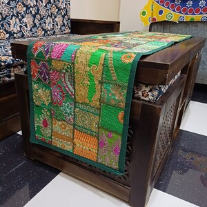 K&ouml;nnte beinhalten: Ein gr&uuml;ner Patchwork-Tischl&auml;ufer mit bunten Stickereien und goldenen Akzenten. Der L&auml;ufer liegt auf einem dunklen Holztisch mit einem geschnitzten Design.