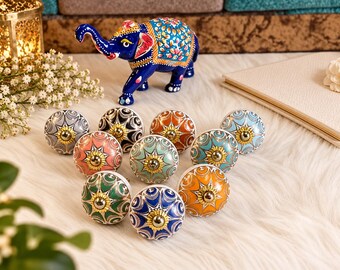 May include: A collection of ten round ceramic cabinet knobs featuring various colorful floral patterns and geometric designs, each centered with a polished gold-tone metal hardware piece, arranged in a triangular formation.
