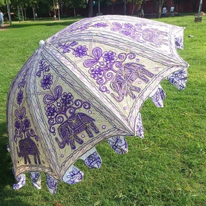 May include: A white and purple umbrella with an embroidered elephant design. The umbrella is open and has a fringe border.