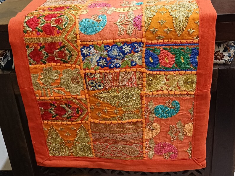 Puede incluir: Un camino de mesa de patchwork colorido con bordados intrincados y detalles de cuentas. El camino de mesa est&aacute; hecho de varias telas en tonos de naranja, rosa, azul y verde. Presenta una variedad de patrones florales y geom&eacute;tricos.