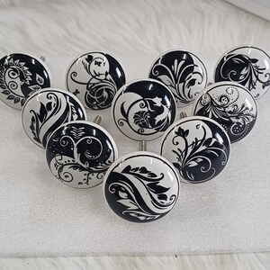 May include: Nine white ceramic cabinet knobs with black floral designs. The knobs have a shiny finish and are perfect for adding a touch of elegance to any room.