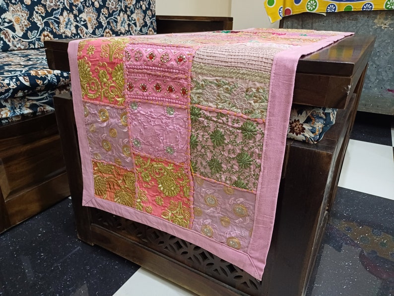 K&ouml;nnte beinhalten: Ein rosa Patchwork-Tischl&auml;ufer mit goldener Stickerei und einem Fransenrand. Der L&auml;ufer besteht aus verschiedenen Stoffen und Texturen und hat einen einzigartigen und bohemischen Stil.