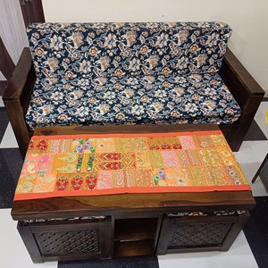 Puede incluir: Un sof&aacute; de madera oscura con un coj&iacute;n de estampado floral y una mesa de caf&eacute; de madera oscura a juego con un corredor de patchwork colorido. La mesa de caf&eacute; tiene dos cajones y un estante abierto.