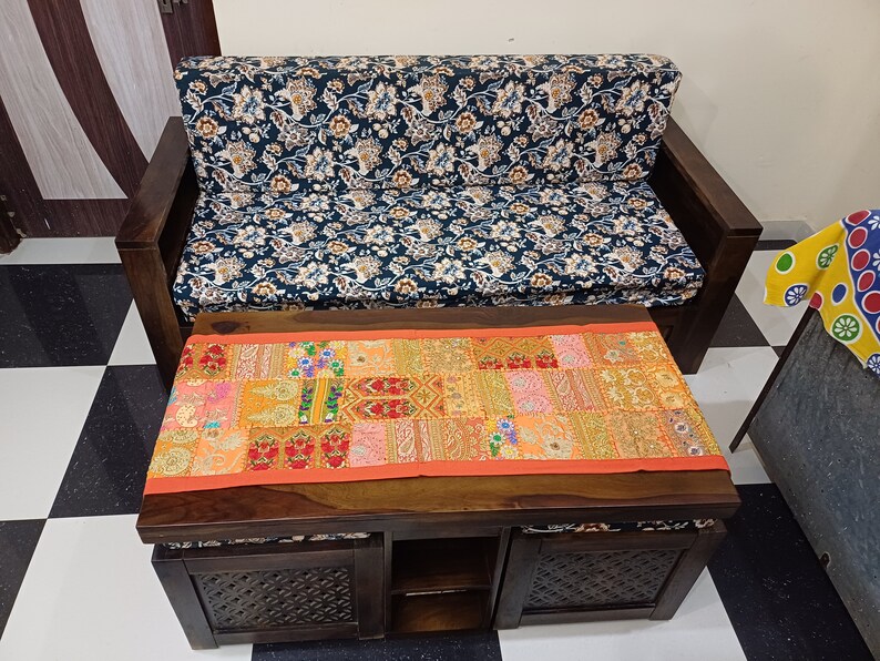 Puede incluir: Un sof&aacute; de madera oscura con un coj&iacute;n de estampado floral y una mesa de caf&eacute; de madera oscura a juego con un corredor de patchwork colorido. La mesa de caf&eacute; tiene dos cajones y un estante abierto.