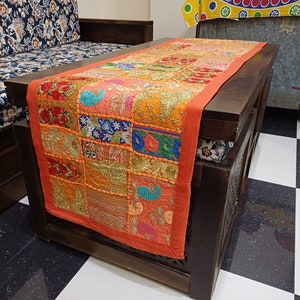Puede incluir: Un camino de mesa de patchwork colorido con acentos naranja, rojo y dorado. El camino de mesa est&aacute; hecho de cuadrados de tela cosidos juntos y presenta intrincados detalles de bordado.