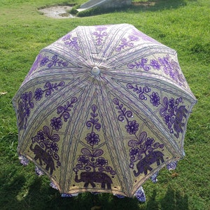 May include: A white and purple umbrella with an embroidered design of elephants and flowers. The umbrella is closed and has a white handle.