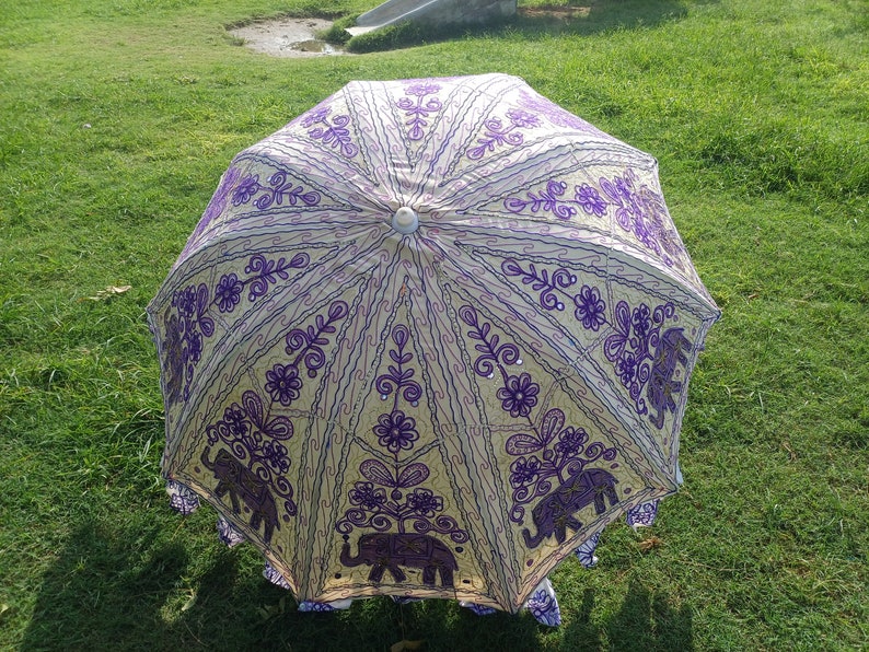 May include: A white and purple umbrella with an embroidered design of elephants and flowers. The umbrella is closed and has a white handle.