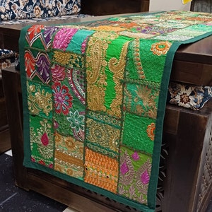 Pode incluir: Um corredor de mesa verde com desenhos de patchwork bordados coloridos. O corredor é feito de tecido com bordados de fio dourado e prateado.