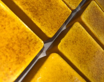 May include: Close-up of multiple rectangular bars of golden yellow soap. The soap has a speckled texture and a shiny surface.