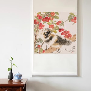 May include: A watercolour painting on a scroll shows a calico cat reaching for red fruit on a tree branch. The artwork features a traditional Asian style with detailed brushstrokes and a soft colour palette. The scroll is white with a wooden roller.
