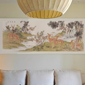 Peut inclure: Un intérieur de salon avec un canapé blanc, une table basse en bois et une grande peinture représentant des cerfs dans un décor forestier. La peinture est encadrée et accrochée au mur au-dessus du canapé. La table basse est décorée de divers objets, dont une théière, des tasses et une petite assiette de fruits. La pièce est décorée dans un style chinois traditionnel.