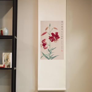 Pode incluir: Uma pintura tradicional chinesa em rolo que representa uma flor de lírio vermelha com folhas verdes. O rolo está montado em um fundo branco e tem uma barra de suspensão na parte superior. A pintura é assinada com caracteres chineses.