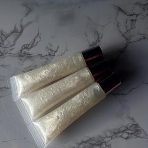 May include: Three clear lip gloss tubes with a pearlescent shimmer. The tubes have rose gold caps.