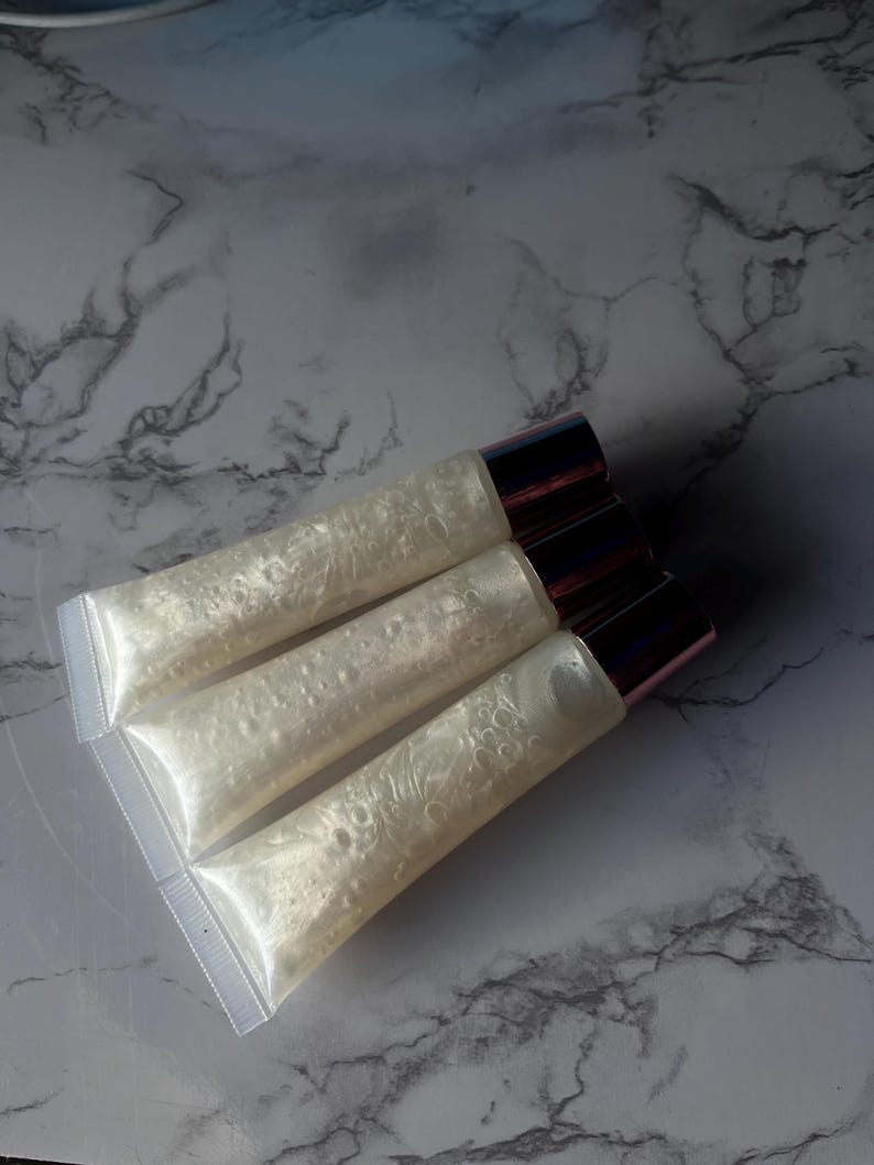 May include: Three clear lip gloss tubes with a pearlescent shimmer. The tubes have rose gold caps.